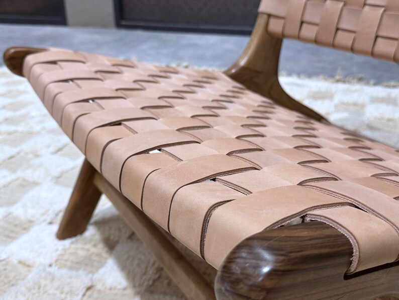 May include: A close-up of a woven leather chair seat. The seat is made of light brown leather straps woven together in a grid pattern. The chair frame is made of dark wood.