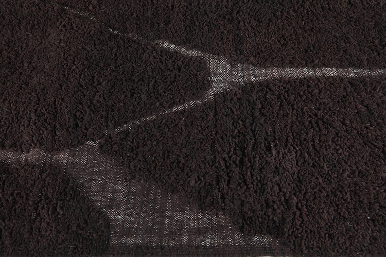 May include: Close-up of a dark brown, textured fabric with a pattern of lighter, white-toned areas. The fabric has a dense, looped pile, creating a soft, plush appearance. The lighter areas create a subtle, abstract design.