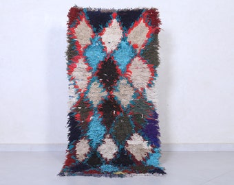 May include: A colorful Moroccan rug with a geometric pattern in shades of red, blue, white, and black. The rug has a distressed, hand-woven look and is made of wool.