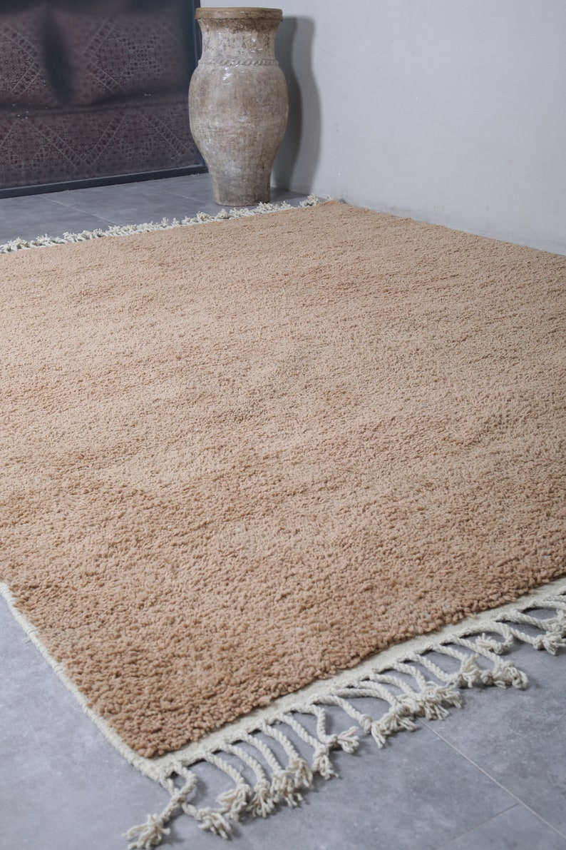 May include: A light brown shag rug with a white fringe border. The rug is on a gray tiled floor.
