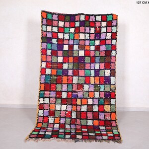May include: A colorful Moroccan rug with a geometric pattern of squares in shades of red, pink, green, blue, and white. The rug is 4.1 feet wide and 7.8 feet long.