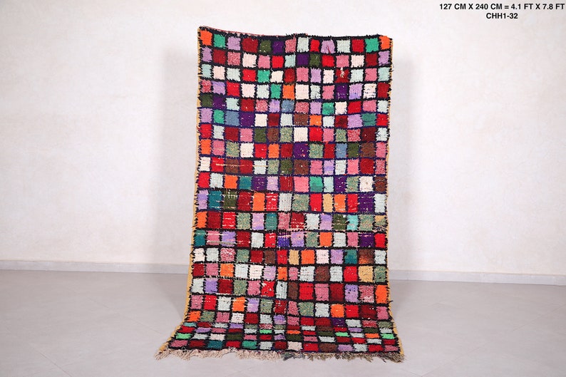 May include: A colorful Moroccan rug with a geometric pattern of squares in shades of red, pink, green, blue, and white. The rug is 4.1 feet wide and 7.8 feet long.