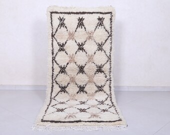 May include: A white and brown Moroccan rug with a diamond pattern. The rug has a fringe border.