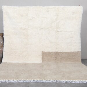 Puede incluir: Una alfombra de pelo blanco y beige con borde de flecos. La alfombra tiene un dise&ntilde;o bicolor con una secci&oacute;n superior blanca y una secci&oacute;n inferior beige.