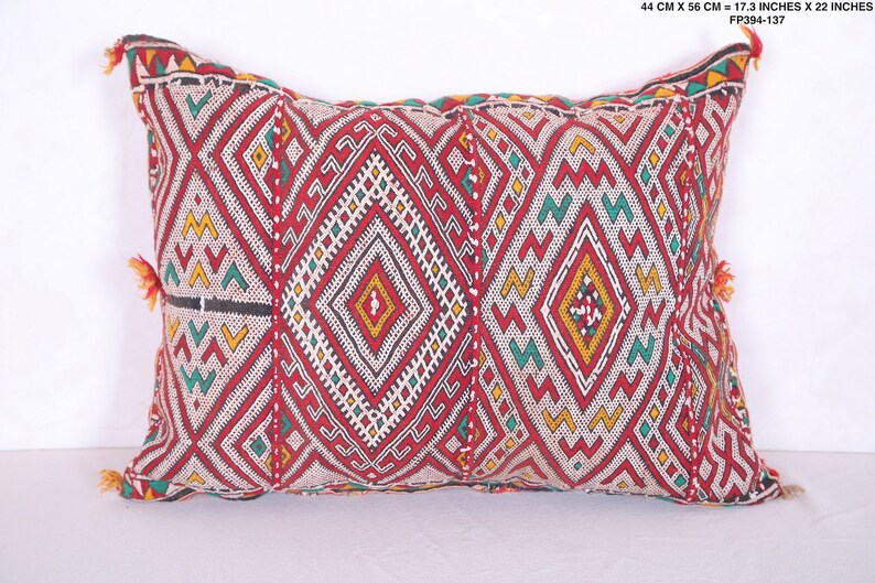 May include: Red, white, green, and yellow geometric patterned throw pillow with tassels. The pillow is 17.3 inches by 22 inches.