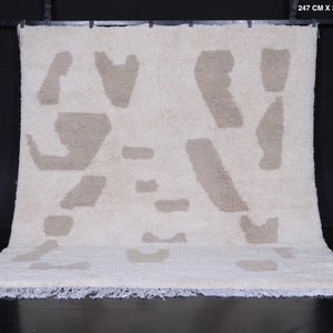 May include: A white rug with a beige abstract pattern. The rug has a fringe border and measures 8.1 feet by 10 feet.