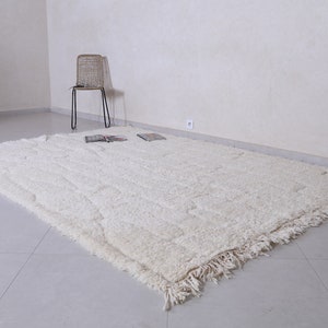 May include: A white shag rug with a fringed border. The rug is laid out on a tiled floor in a room with white walls.