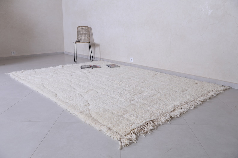 May include: A white shag rug with a fringed border. The rug is laid out on a tiled floor in a room with white walls.