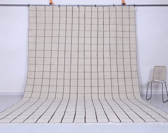 May include: A large, off-white rug with a black grid pattern. The rug is hanging on a wall and is draped over a chair.