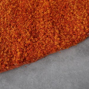 May include: Close-up of a round, orange and brown shag rug. The rug has a soft, fluffy texture.