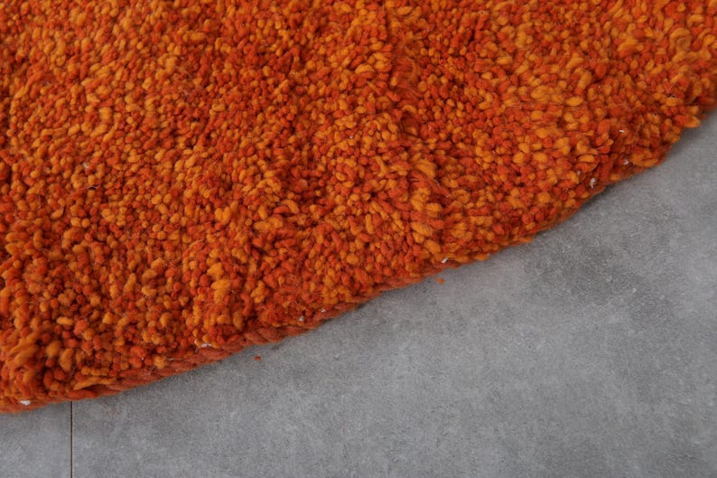 May include: Close-up of a round, orange and brown shag rug. The rug has a soft, fluffy texture.
