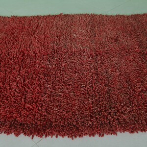 May include: A close-up of a red shag rug with a soft, fluffy texture.