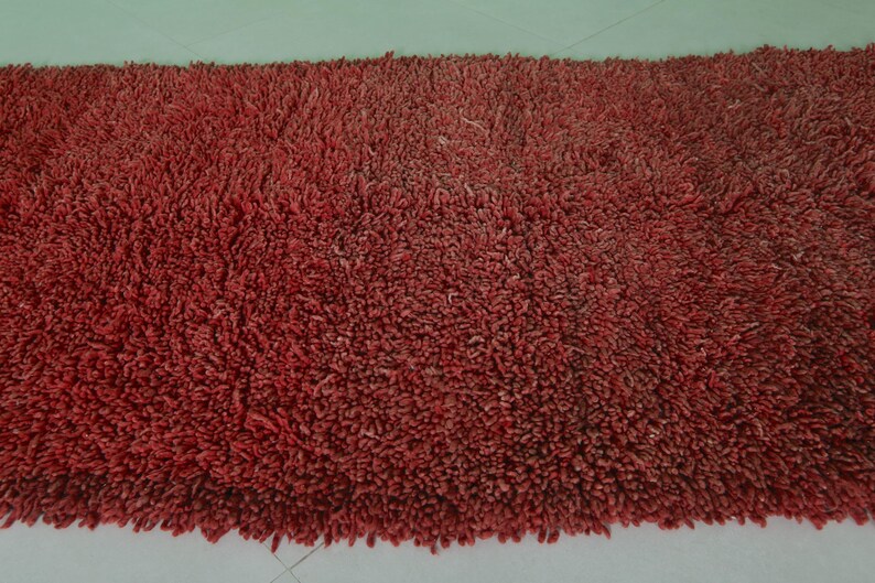 May include: A close-up of a red shag rug with a soft, fluffy texture.