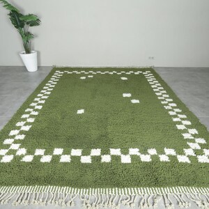 May include: A rectangular green rug with a white checkered border and fringe. The rug has a plush texture and a simple design, suitable for a living room or bedroom. The rug measures approximately 60 inches by 90 inches.