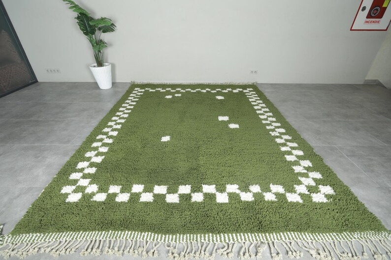 May include: A rectangular green rug with a white checkered border and fringe. The rug has a plush texture and a simple design, suitable for a living room or bedroom. The rug measures approximately 60 inches by 90 inches.