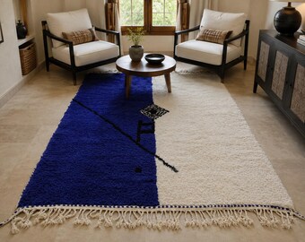 Puede incluir: Una alfombra rectangular con un diseño dividido, una mitad en azul profundo y la otra en blanco roto. La alfombra tiene un pelo grueso y texturizado, un patrón de líneas diagonales negras y flecos decorativos anudados en los bordes.