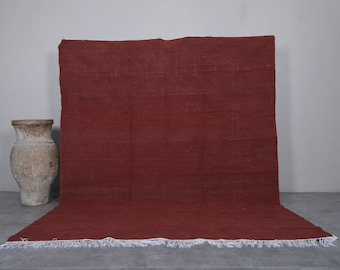 May include: A solid rust-colored rug with a white fringe border. The rug is laid out flat on a gray floor.