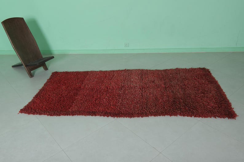 May include: A red shag rug with a long rectangular shape. The rug is on a light-colored floor.