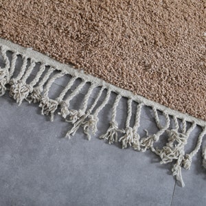 May include: A brown rug with a fringe border. The rug is made of a soft, fluffy material.