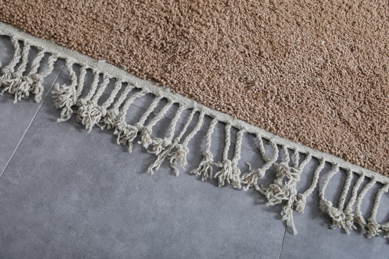 May include: A brown rug with a fringe border. The rug is made of a soft, fluffy material.