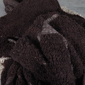 May include: A dark brown, textured throw blanket with a shaggy appearance. The blanket has a woven backing and a cream-colored fringe along the edges. The fabric appears soft and plush.