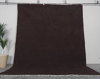 May include: A dark brown rug with a fringe border. The rug is hanging on a wall and is made of a soft, plush material.