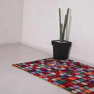 May include: A colorful, geometric patterned rug with a black planter and a tall, green cactus plant in a white corner.