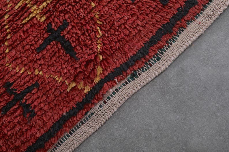 May include: Close-up of a red, black, and gold patterned rug with a fringe border. The rug is made of a thick, textured material.