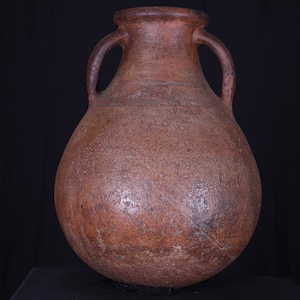 Può includere: Un'ampia brocca di terracotta marrone con due manici. La brocca ha un corpo rotondo e un collo stretto.