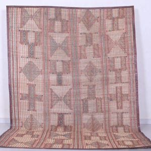 May include: A rectangular woven mat with a geometric pattern in shades of beige, red, and brown. The design features repeating shapes including crosses, diamonds, and triangles. The mat has a dark brown border.