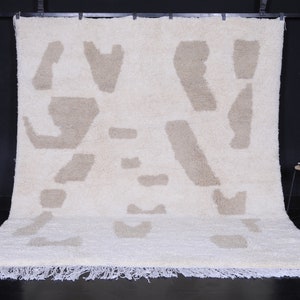 May include: A white shag rug with a beige abstract pattern. The rug has a fringe border.