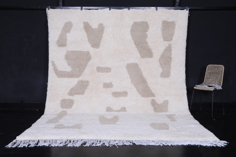 May include: A white shag rug with a beige abstract pattern. The rug has a fringe border.