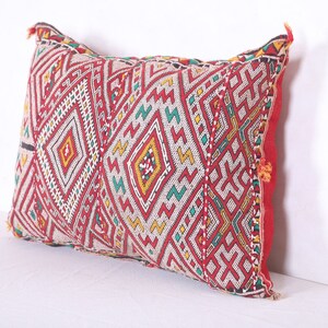 May include: A rectangular pillow with a red, white, green, and yellow geometric pattern. The pillow is made of a woven fabric and has a fringe border.
