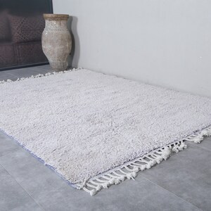 K&ouml;nnte beinhalten: Ein wei&szlig;er, flauschiger Teppich mit Fransenrand. Der Teppich liegt auf einem Fliesenboden.