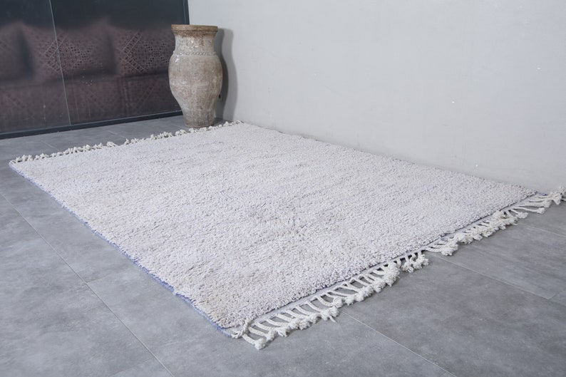 K&ouml;nnte beinhalten: Ein wei&szlig;er, flauschiger Teppich mit Fransenrand. Der Teppich liegt auf einem Fliesenboden.