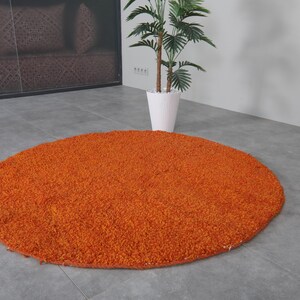 May include: A round, orange shag rug on a gray floor.