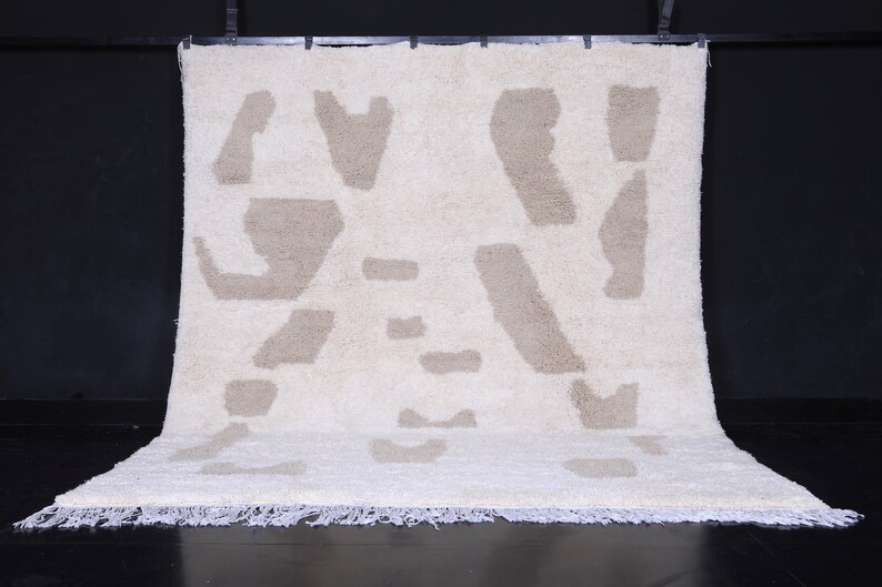 May include: A white and beige shag rug with an abstract pattern. The rug has a fringe border.