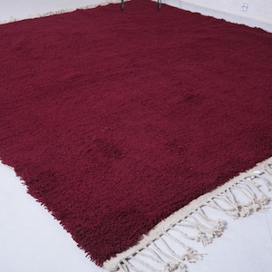 May include: A burgundy shag rug with a white fringe border. The rug is made of soft, plush fibers and has a luxurious feel.