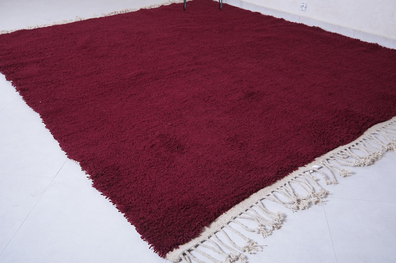May include: A burgundy shag rug with a white fringe border. The rug is made of soft, plush fibers and has a luxurious feel.