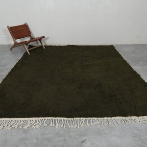 May include: A dark green shag rug with a white fringe border. The rug is laid out on a gray tiled floor.