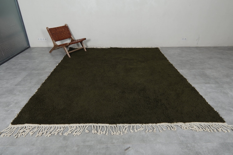 May include: A dark green shag rug with a white fringe border. The rug is laid out on a gray tiled floor.