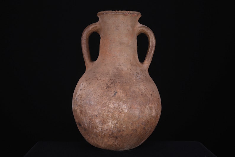 Puede incluir: Una jarra de cer&aacute;mica de terracota marr&oacute;n con dos asas. La jarra tiene un cuerpo redondeado y un cuello estrecho.
