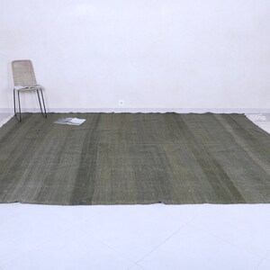 May include: A green woven rug with a white fringe border. The rug is laid out on a white tiled floor.