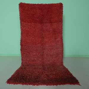 May include: A deep red shag rug with a long pile. The rug is laid out flat on a light green floor.
