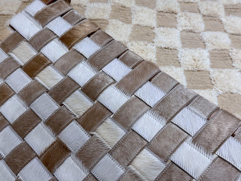 May include: A woven leather ottoman with a chequered pattern. The ottoman is made of light brown and white leather strips.