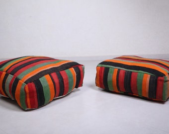 May include: Two colorful striped floor cushions with a rectangular shape. The cushions are made of a woven fabric with red, orange, green, black, and white stripes.