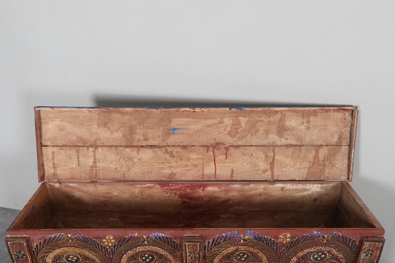 May include: An antique wooden chest with the lid open, revealing the interior. The chest is painted in shades of red, gold, and blue, with ornate floral and geometric designs. The interior is made of light-coloured wood.