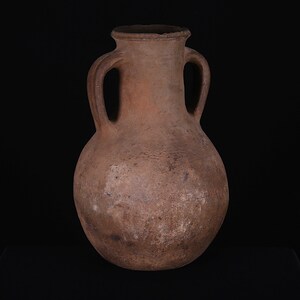 Puede incluir: Una jarra de barro marr&oacute;n con dos asas. La jarra tiene un cuerpo redondeado y un cuello estrecho.