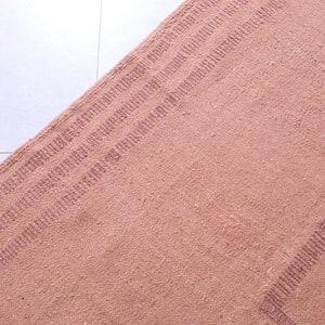 May include: A close-up of a pink woven rug with a subtle striped pattern. The rug has a textured surface and a slightly faded appearance.