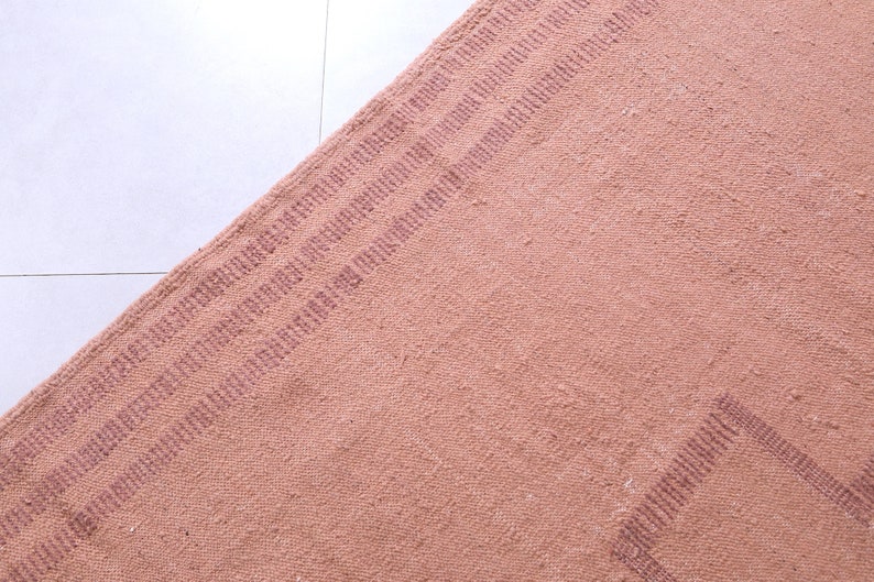 May include: A close-up of a pink woven rug with a subtle striped pattern. The rug has a textured surface and a slightly faded appearance.